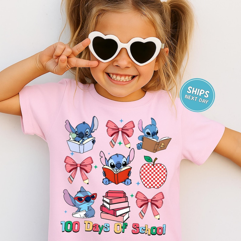 A young girl wearing a pink t-shirt with a cartoon character design and heart-shaped sunglasses, smiling and making a peace sign.