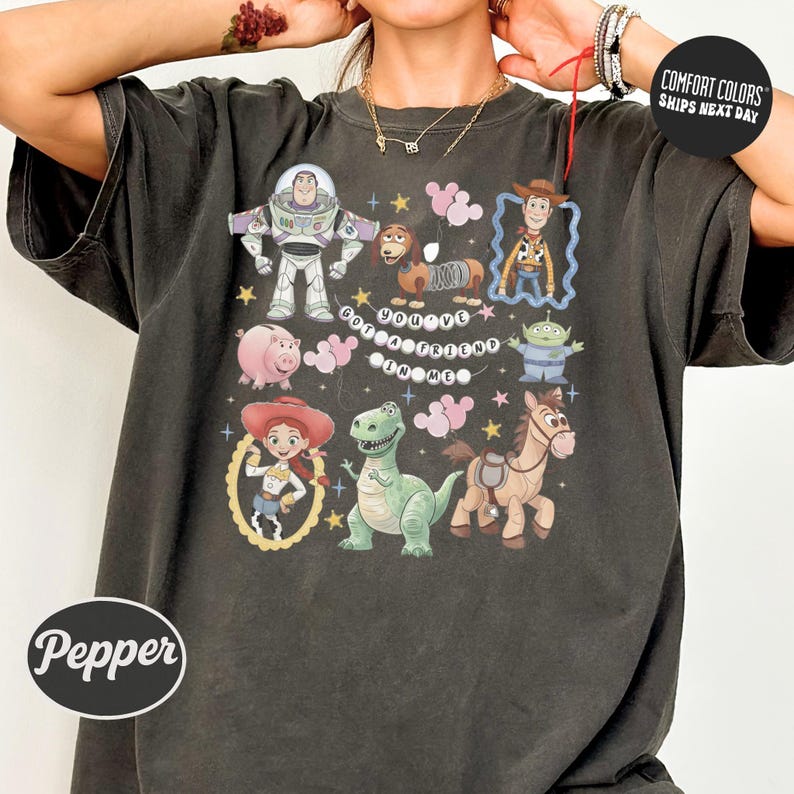 A person wearing a black t-shirt with a graphic design featuring characters from the Toy Story movie, including Buzz Lightyear, Woody, and other beloved characters.