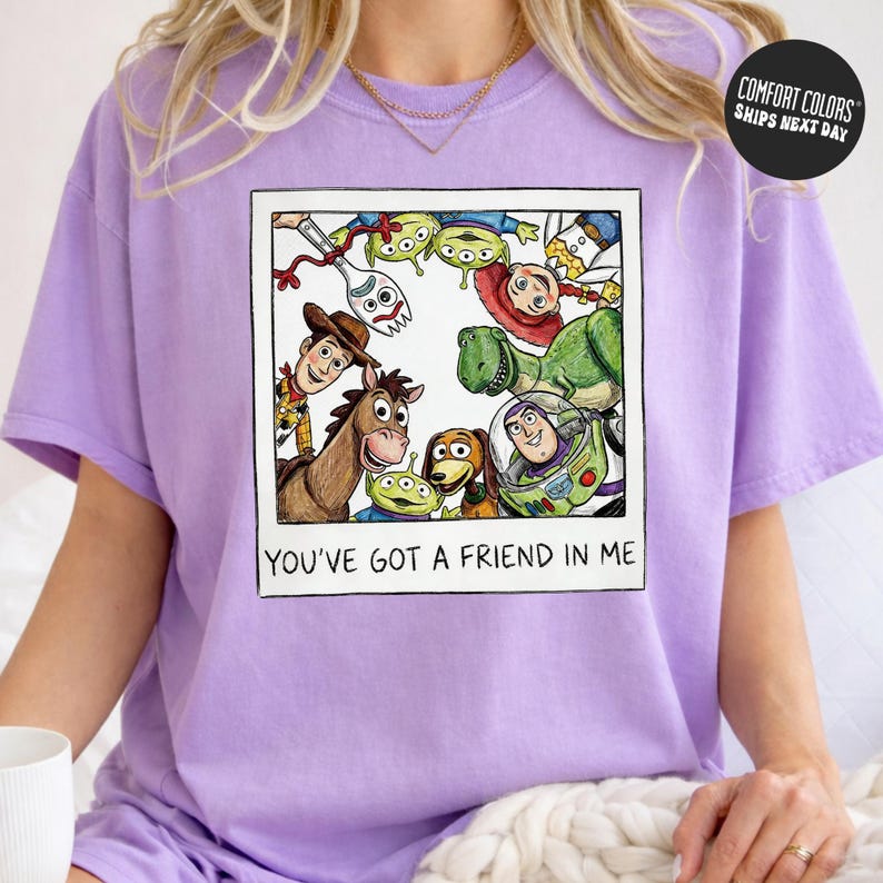 A person wearing a purple t-shirt with a graphic of characters from the Toy Story franchise, including Woody, Buzz Lightyear, and other beloved characters, along with the text "You've Got a Friend in Me".