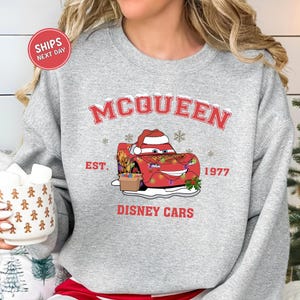 A gray sweatshirt with a graphic of a red car wearing a Santa hat and the text "McQueen" and "Disney Cars" printed on it.