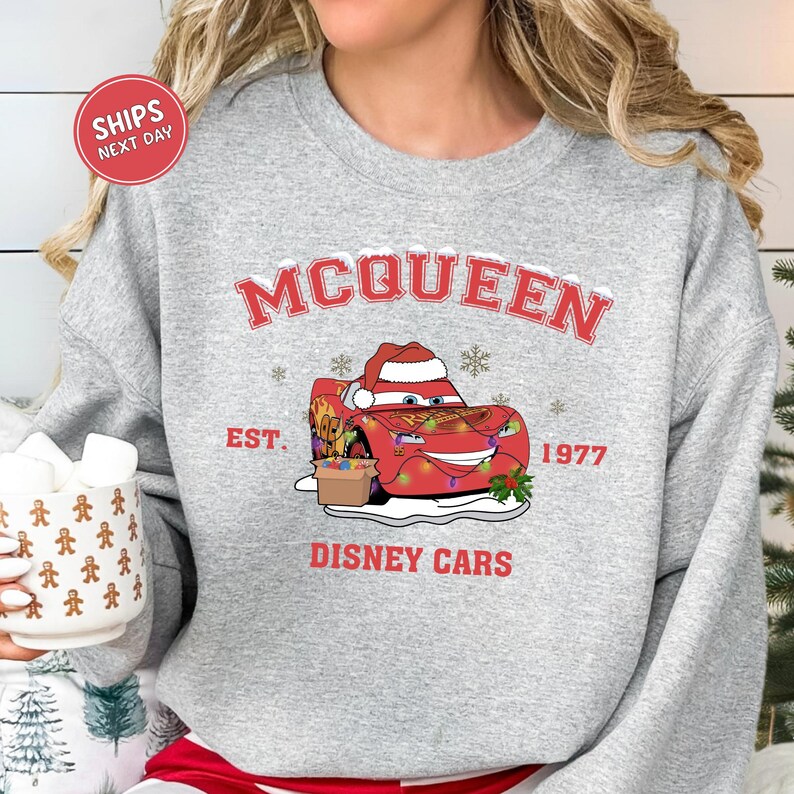A gray sweatshirt with a graphic of a red car wearing a Santa hat and the text "McQueen" and "Disney Cars" printed on it.