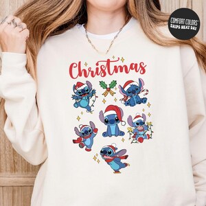 A woman wearing a white sweatshirt with a Christmas-themed design featuring cartoon characters of Stitch from the Lilo & Stitch movie.