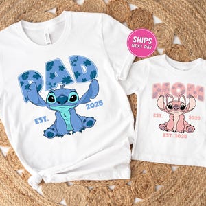 two white t-shirts with a design of a blue cartoon character, likely a character from the popular animated series "Stitch". The t-shirts are labeled with the text "PAD" and "MOM", indicating they are intended for a father and mother. The t-shirts are displayed on a woven mat, and there is a pink shipping label in the top right corner, suggesting that the t-shirts are being shipped.