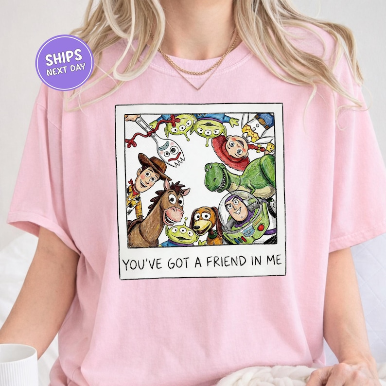 A pink t-shirt with a graphic design featuring characters from the Toy Story franchise, including Woody, Buzz Lightyear, and other beloved characters.