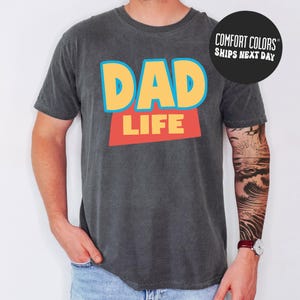 A man wearing a gray t-shirt with the text "DAD LIFE" printed on it.