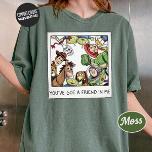 A person wearing a green t-shirt with a graphic design featuring characters from the Toy Story movie, including Woody, Buzz Lightyear, and other beloved characters.