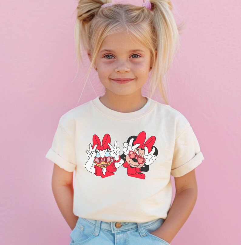 A young girl with blonde hair is smiling and wearing a white t-shirt with a graphic of Minnie Mouse and Mickey Mouse.