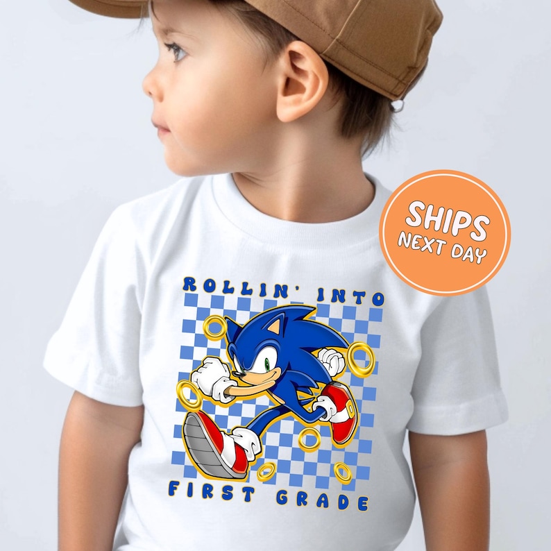 A young child wearing a white t-shirt with a graphic of Sonic the Hedgehog and the text "Rollin' into first grade" printed on it.