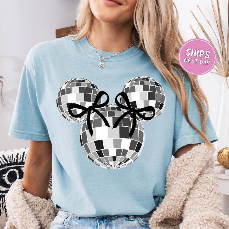 A woman wearing a light blue t-shirt with a graphic of a disco ball and two black bows.