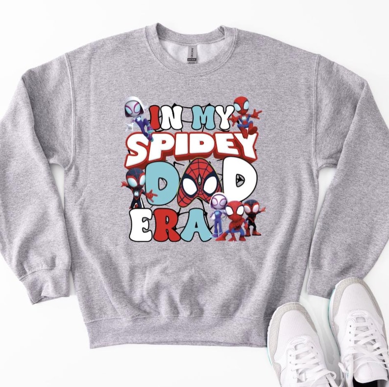 A gray sweatshirt with a graphic design featuring various Spider-Man characters and the text "IN MY SPIDERY DAD ERA" printed on it.