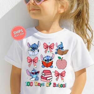 A young girl wearing a white t-shirt with a graphic design featuring various cartoon characters and school-related icons, such as books, apples, and bows.