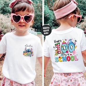 A young girl wearing a white t-shirt with a personalized design and text, standing in a garden setting.