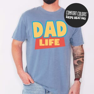 A man wearing a blue t-shirt with the text "DAD LIFE" printed on it.