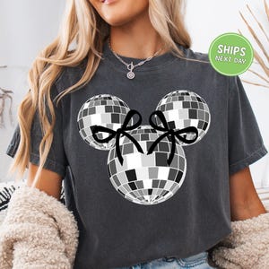 A woman wearing a gray t-shirt with a graphic of a disco ball and two black bows.