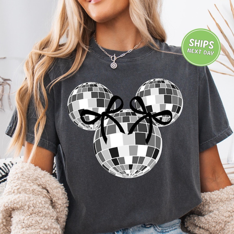 A woman wearing a gray t-shirt with a graphic of a disco ball and two black bows.