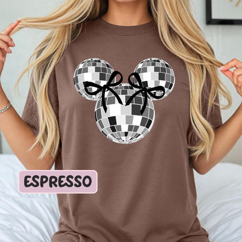 A woman wearing a brown t-shirt with a graphic of a disco ball and two black bows.