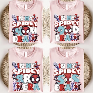 four pink t-shirts with the text "IN MY SPIDERY MOM ERA" printed on them. The shirts are arranged in a grid-like pattern, with each shirt placed on top of a woven basket.