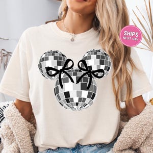 A woman wearing a white t-shirt with a graphic of a disco ball and two black bows.