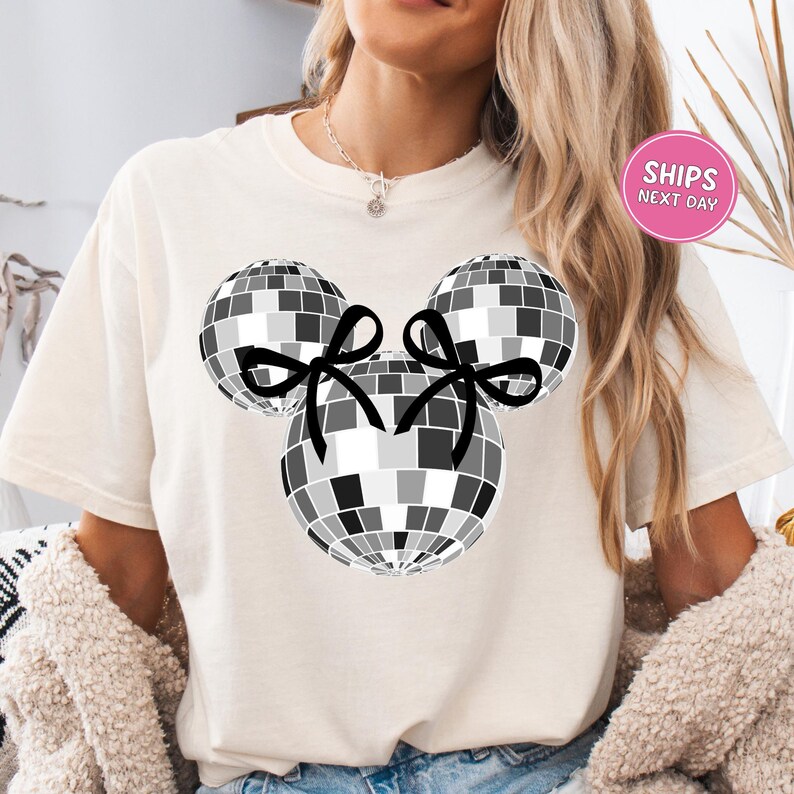 A woman wearing a white t-shirt with a graphic of a disco ball and two black bows.