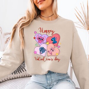 A woman wearing a beige sweatshirt with a graphic design featuring cartoon characters and the text "Happy Valentine's day".