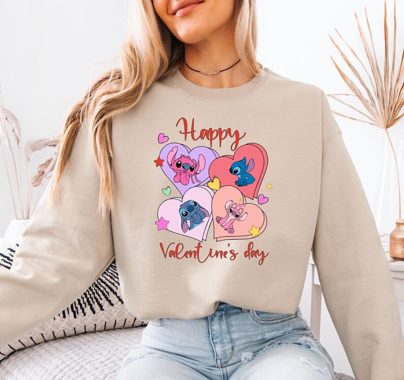 A woman wearing a beige sweatshirt with a graphic design featuring cartoon characters and the text "Happy Valentine's day".