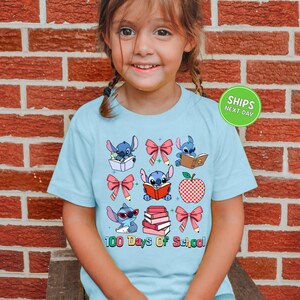 A young girl wearing a light blue t-shirt with a graphic design of various cartoon characters and text related to school.