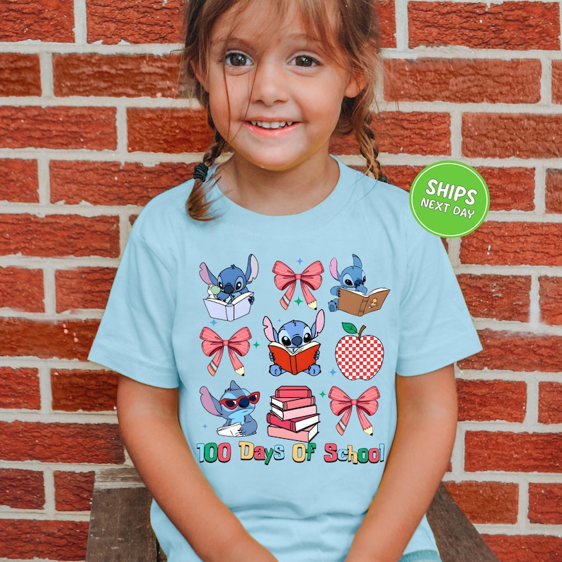A young girl wearing a light blue t-shirt with a graphic design of various cartoon characters and text related to school.