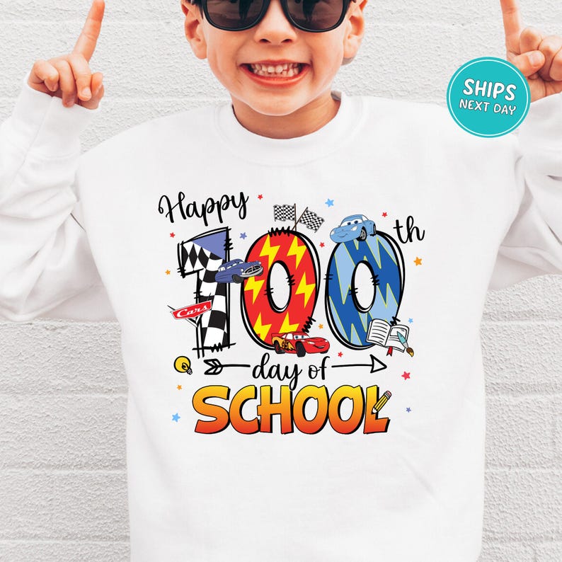 A young boy wearing a white sweatshirt with a colorful graphic design celebrating the 100th day of school.