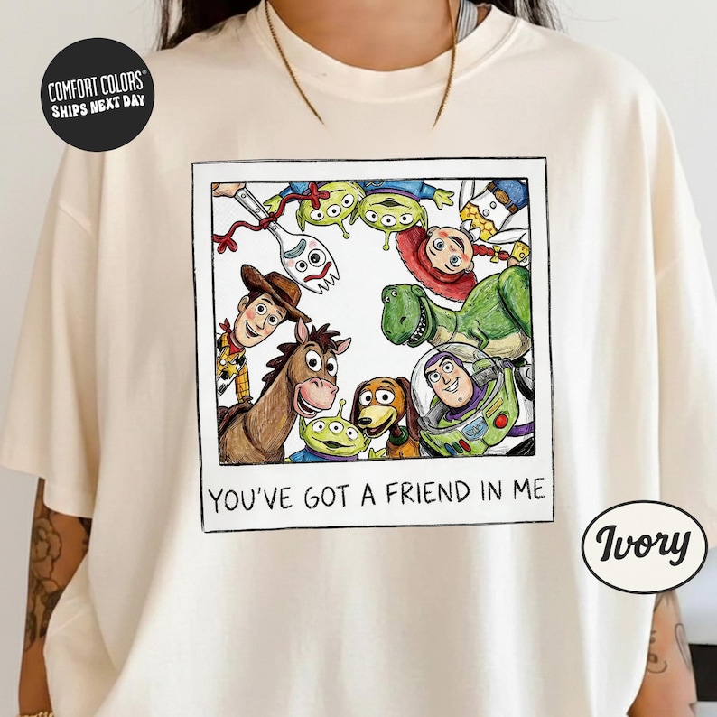 A person wearing a white t-shirt with a graphic design featuring characters from the Toy Story franchise, including Woody, Buzz Lightyear, and other beloved characters.