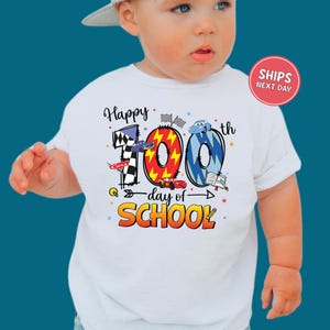 A baby wearing a white t-shirt with a colorful graphic design celebrating the 100th day of school.