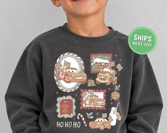 May include: A charcoal grey crewneck sweatshirt featuring a festive graphic print of cartoon race cars, a chimney, a mailbox labelled Letters for Santa, a candy cane, a cookie, and a milk bottle, with the text Ho Ho Ho printed at the bottom.