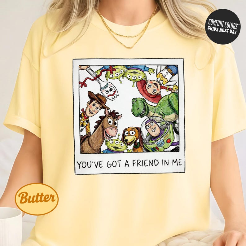 A yellow t-shirt with a graphic design featuring characters from the Toy Story franchise, including Woody, Buzz Lightyear, and other beloved characters. The text on the t-shirt reads "You've Got a Friend in Me".