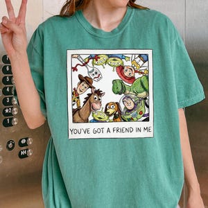 A person wearing a green t-shirt with a graphic of characters from the Toy Story movie, including Woody, Buzz Lightyear, and other beloved characters, along with the text "You've Got a Friend in Me".