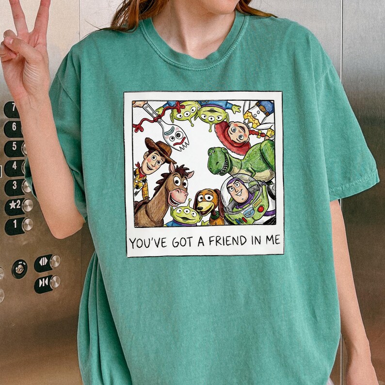 A person wearing a green t-shirt with a graphic of characters from the Toy Story movie, including Woody, Buzz Lightyear, and other beloved characters, along with the text "You've Got a Friend in Me".