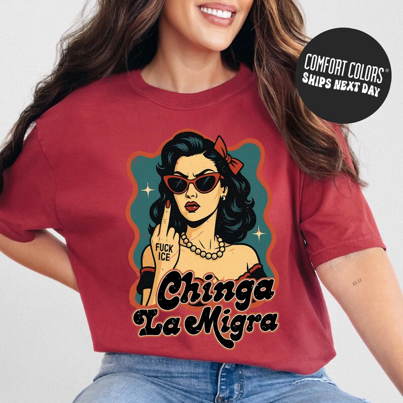 A woman wearing a red t-shirt with a graphic design featuring a woman with sunglasses and the text "Chinga La Migra" (Spanish for "I'm not a chink").