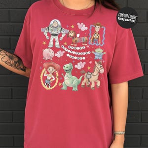 A person wearing a red t-shirt with a graphic design featuring characters from the Toy Story franchise, including Buzz Lightyear, Woody, and other beloved characters.