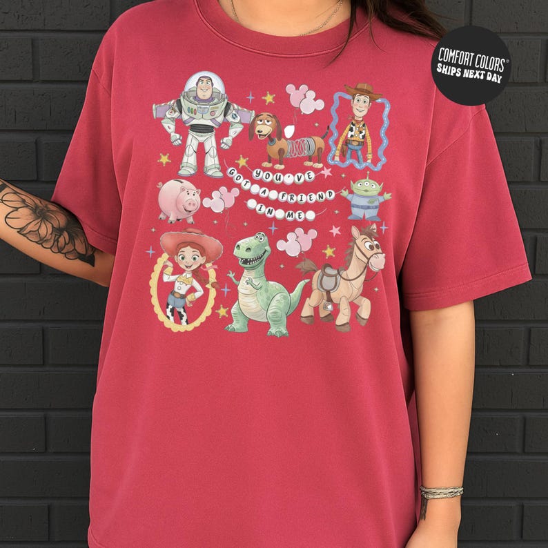 A person wearing a red t-shirt with a graphic design featuring characters from the Toy Story franchise, including Buzz Lightyear, Woody, and other beloved characters.