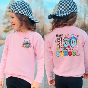 A young girl wearing a pink sweatshirt with a cartoon character and text printed on it, standing outdoors.