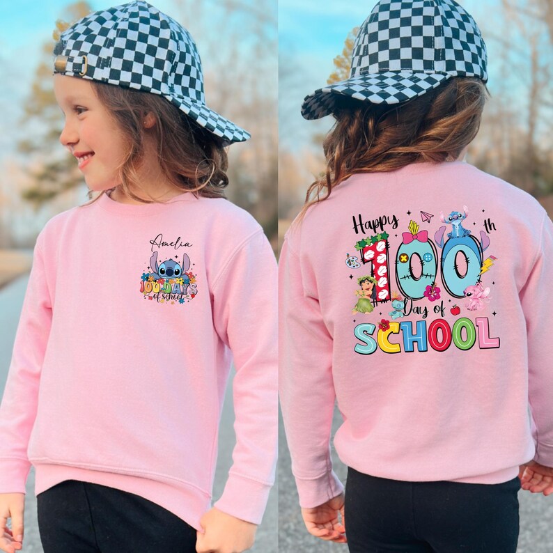 A young girl wearing a pink sweatshirt with a cartoon character and text printed on it, standing outdoors.