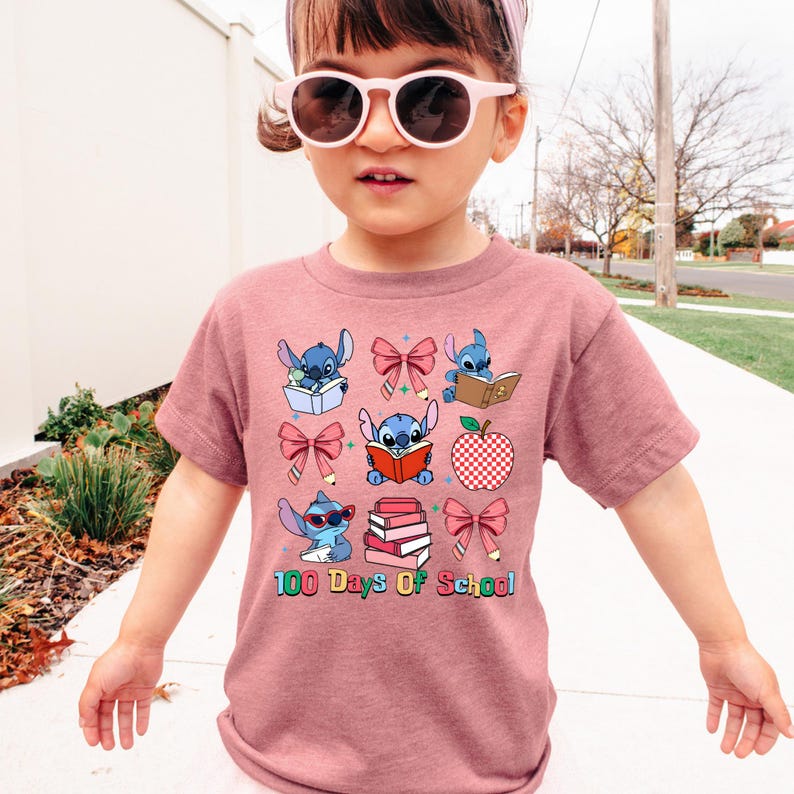 A young girl wearing a pink t-shirt with a graphic design of cartoon characters and text, standing on a sidewalk.