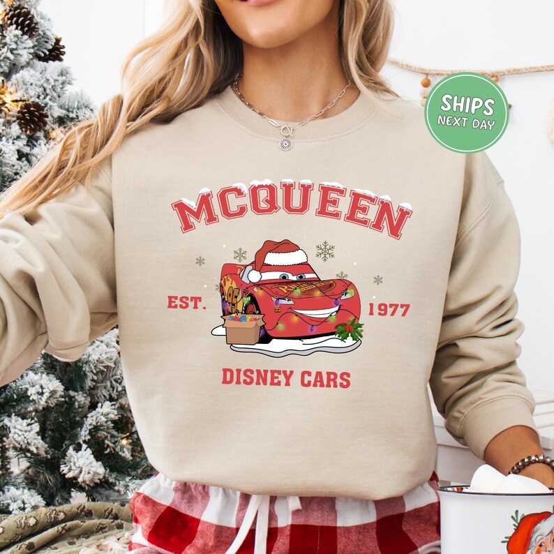 A woman wearing a beige sweatshirt with a graphic of a red car and the text "McQueen" and "Disney Cars" printed on it.