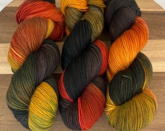 May include: Six skeins of colorful yarn in shades of orange, yellow, and black are arranged on a wooden surface. The yarn is tightly wound, showcasing a gradient of colors. The yarn appears to be soft and suitable for knitting or crocheting projects.