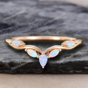May include: A gold ring with a curved design, featuring five opal gemstones. The opals are pear and marquise-shaped, displaying iridescent colours. The ring's band is smooth and polished.