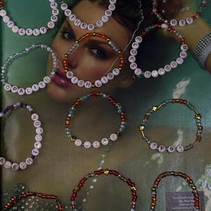 May include: A collection of beaded bracelets with white letter beads spelling out various words. The bracelets are in shades of red, gold, and clear beads. Some bracelets have star-shaped accents. The background is a magazine page.