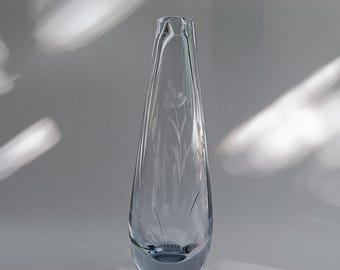 Op de afbeelding: Een heldere glazen vaas met een druppelvorm. De vaas heeft een geëtst bloemmotief aan de voorkant. De vaas staat op een wit oppervlak met schaduwen. Ongeveer 25 cm hoog.