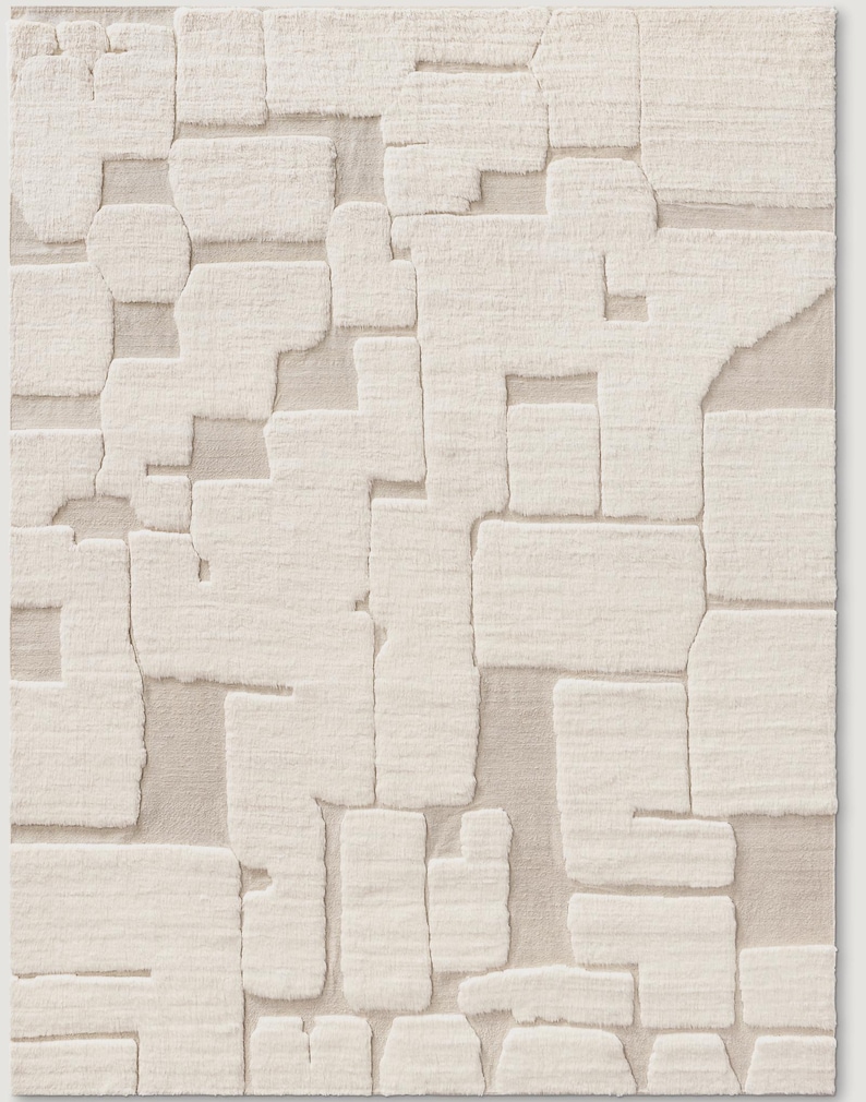 Puede incluir: Una alfombra rectangular de color blanquecino con un patr&oacute;n geom&eacute;trico texturizado. El dise&ntilde;o presenta formas irregulares en relieve que se asemejan a bloques o piezas de rompecabezas, creando una superficie t&aacute;ctil. La paleta de colores neutros y el dise&ntilde;o abstracto la hacen adecuada para varios estilos de interior.
