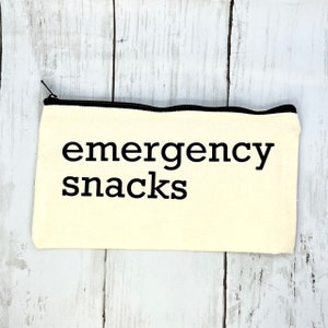 May include: A white canvas zippered pouch with black trim and the text "emergency snacks" printed in black.