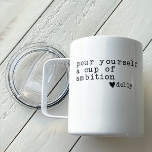 May include: White ceramic mug with a black handle and a black lid. The mug has the text "pour yourself a cup of ambition &hearts; dolly" printed on it.
