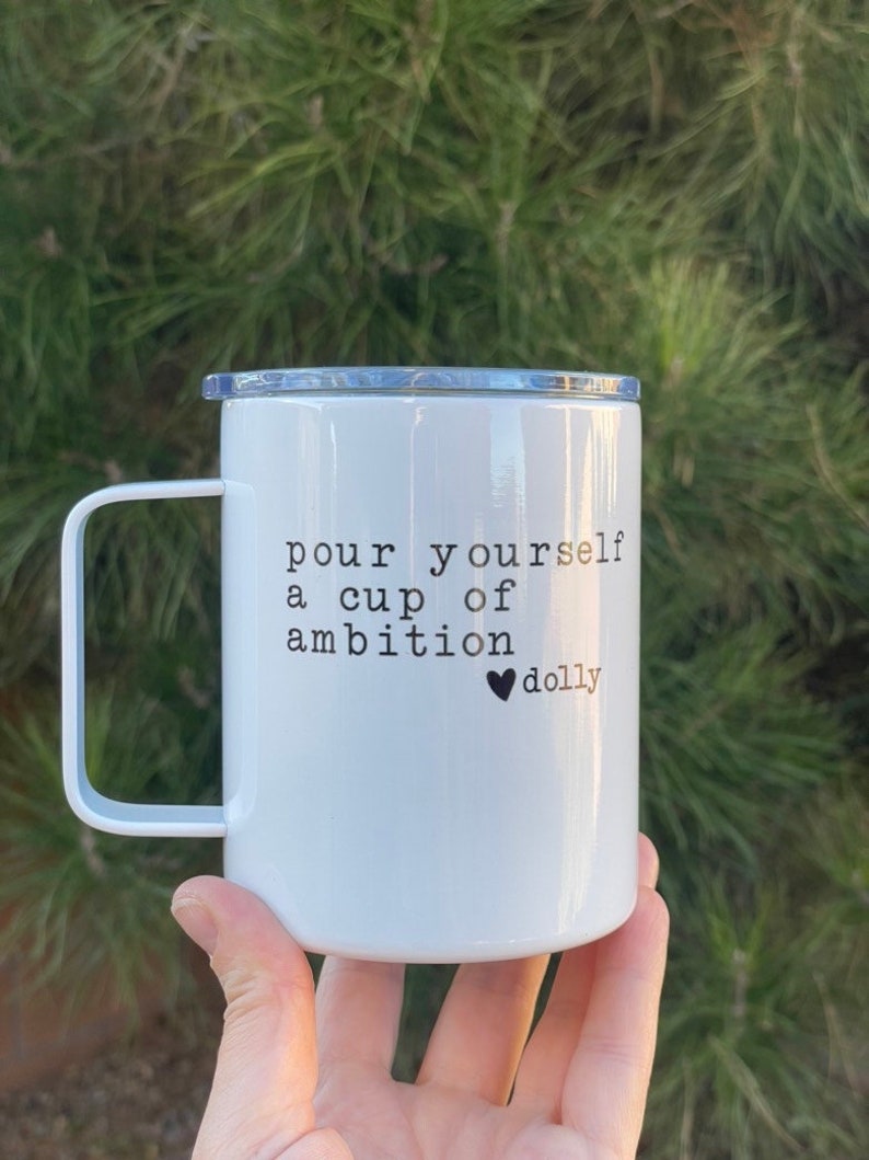 May include: White ceramic mug with a black handle and a black inscription that reads "pour yourself a cup of ambition &hearts;dolly".
