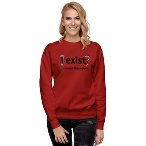 May include: A red sweatshirt featuring the text "I exist?" in a unique font. The words "between Question" are printed below. The long-sleeved sweatshirt is worn by a person.